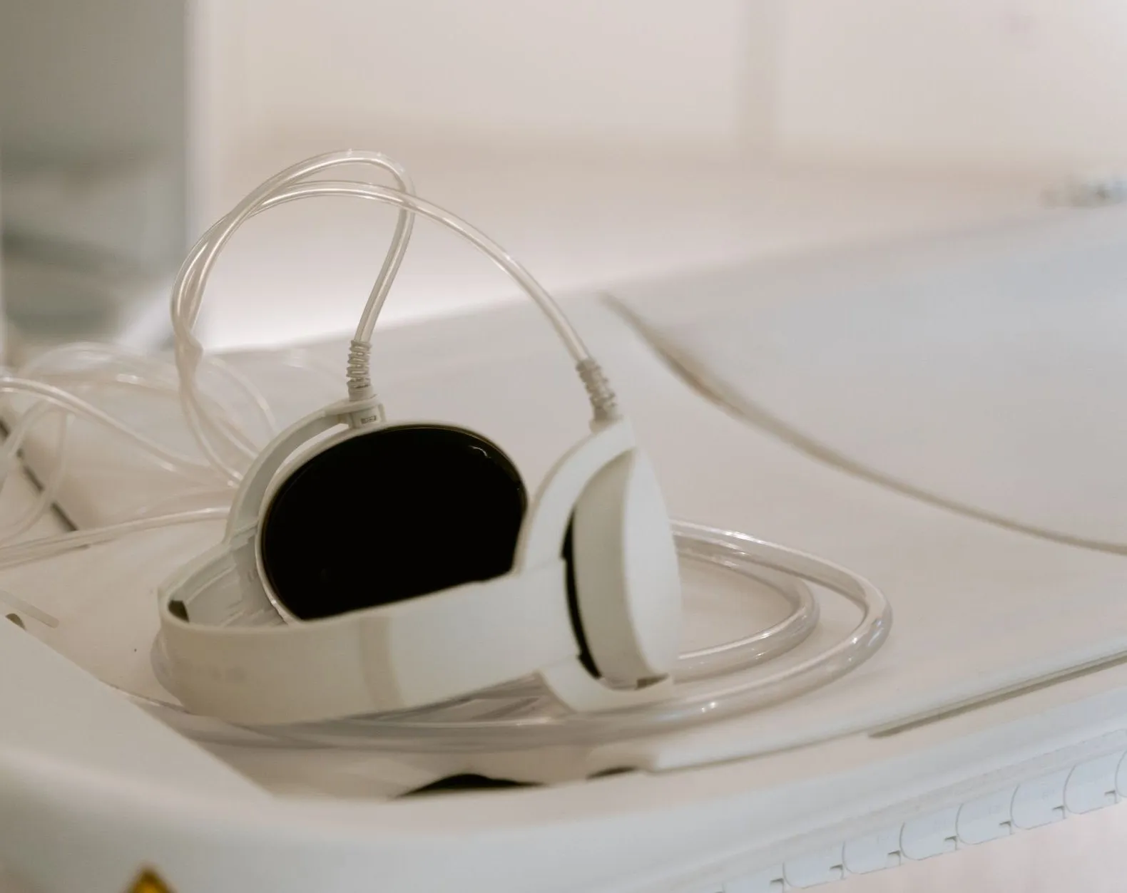 White audiometry headphones with their clear cable coiled on a pale clinic shelf