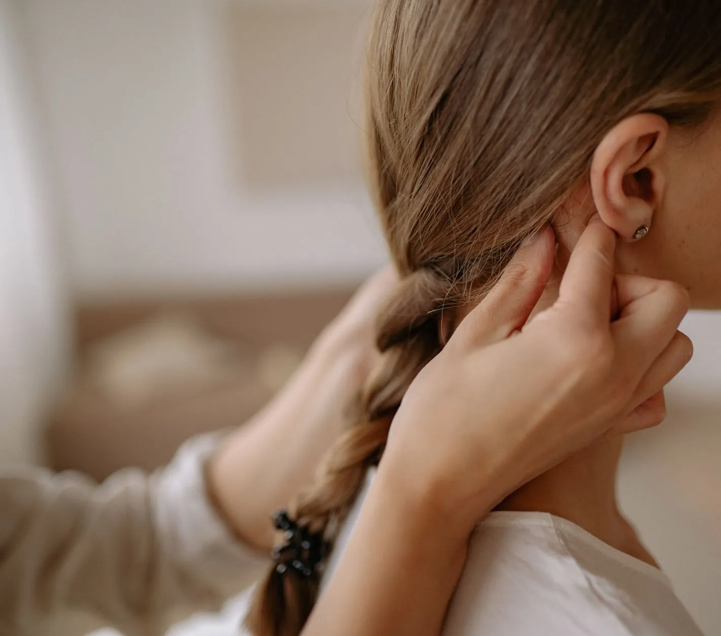 An audiologist's hands at a patient's ear during a fitting, the patient's plait falling over her shoulder